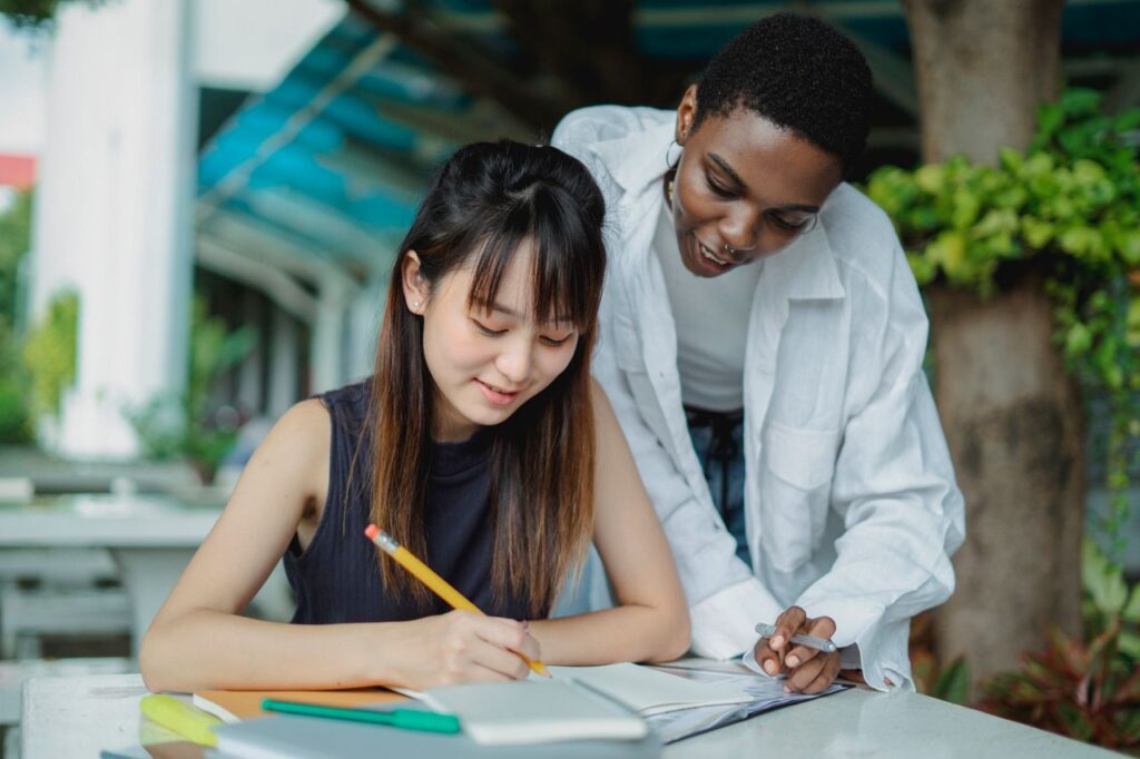 Young multiracial female students in casual clothes studying outside with books in summer day in park
